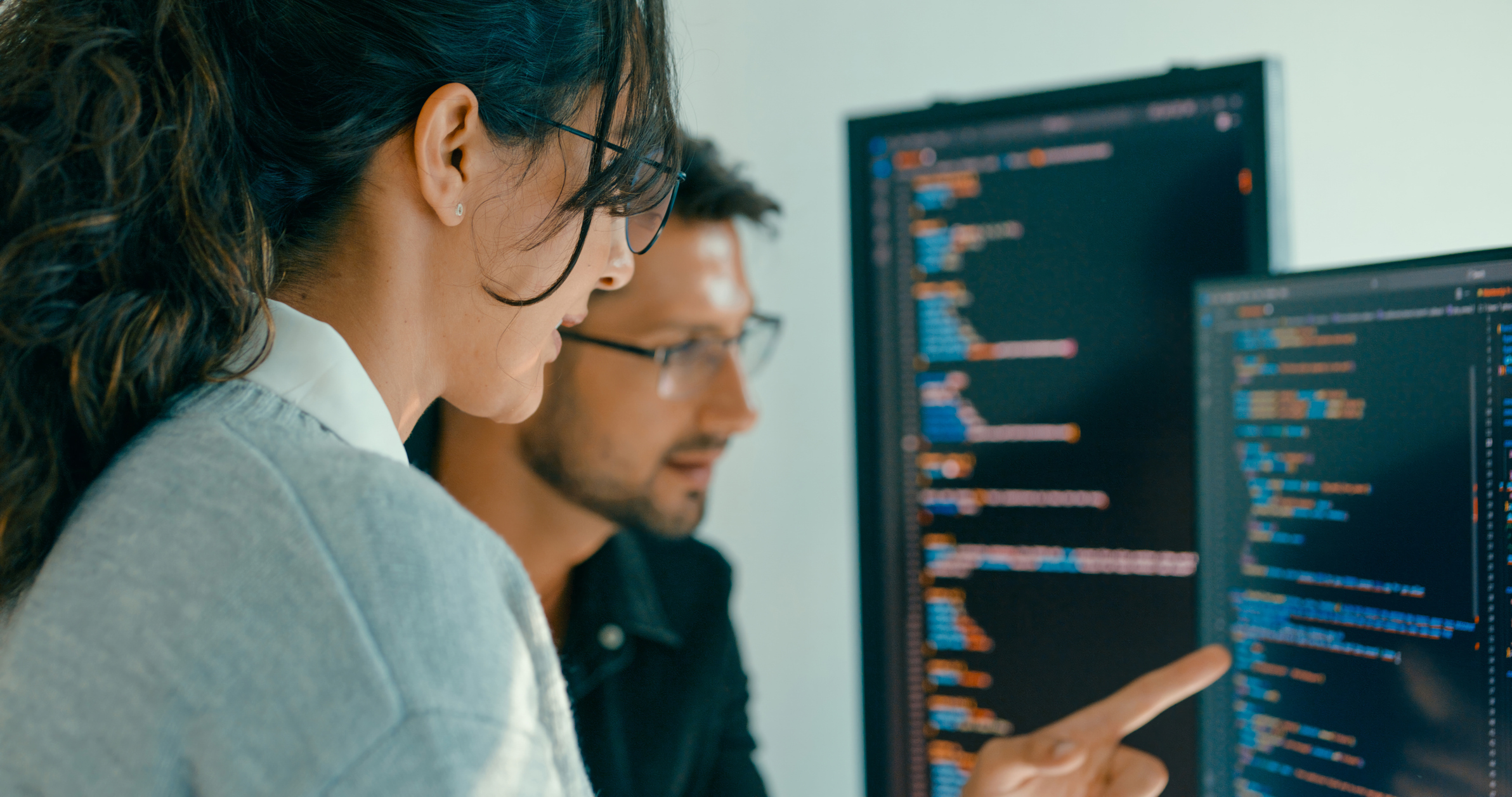 Two coworkers viewing code on a desktop